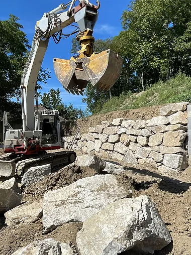 Bagger setzt Natursteine für Böschungssicherung