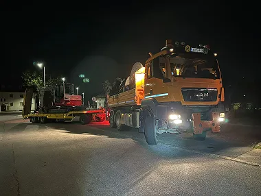 Tieflader mit Bagger beim Maschinentransport bei Nacht